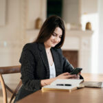 A woman sitting at a table, looking at her phone.