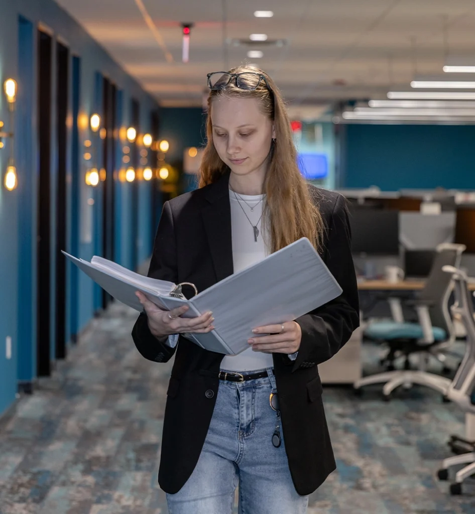 Woman reading documents in an office hallway.
